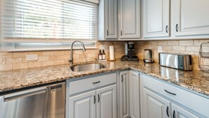 A kitchen with light blue cabinets, a granite countertop, a dishwasher, a coffee maker, and a toaster. - Modern North Potomac Home w/ Furnished Deck! (Gaithersburg)