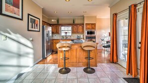 Una cocina con dos taburetes, un refrigerador, un horno y una ventana con cortinas.