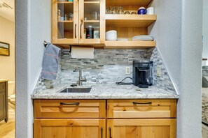 Une cuisine compacte avec des meubles en bois, un plan de travail en marbre, une machine à café et un dosseret carrelé.
