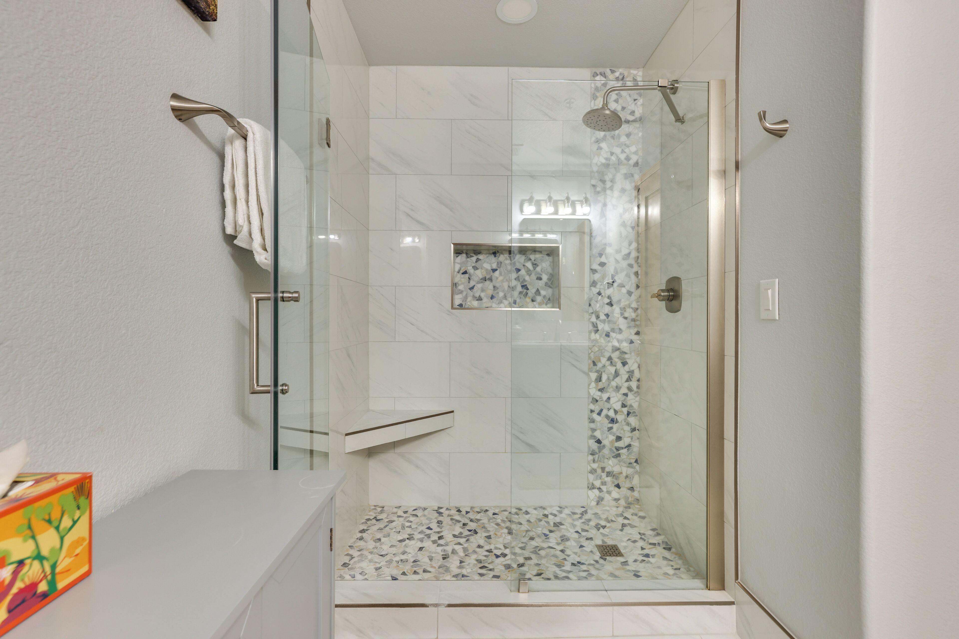 Un bagno moderno con cabina doccia in vetro, un lavandino bianco e pavimento doccia piastrellato.
