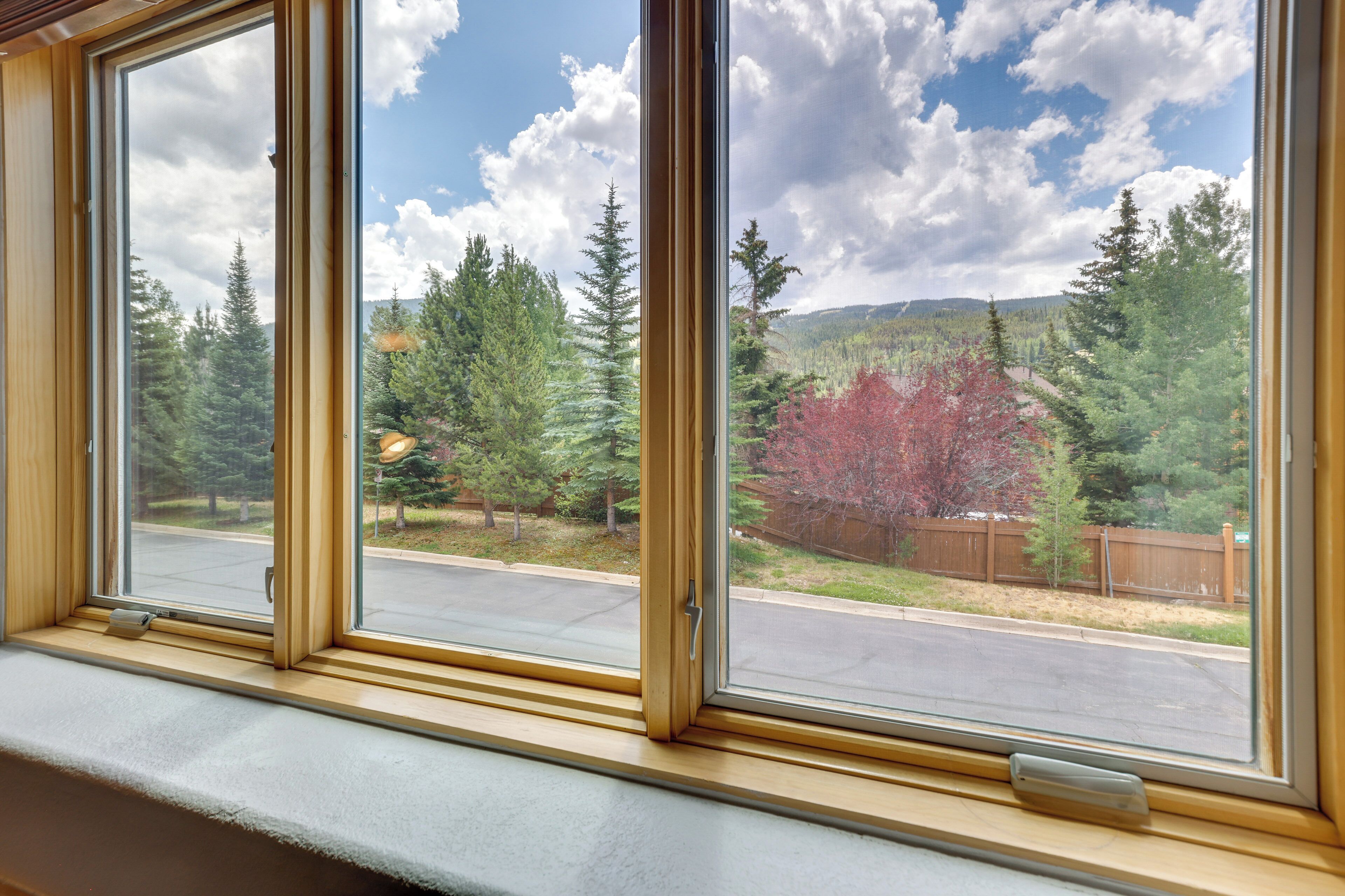 A window with a view of a road, trees, and a mountain range.