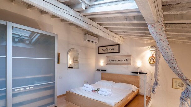 A bedroom with a wooden bed, a sliding glass door, and a ceiling with exposed beams. - Modern Murate View in Florence by Mmega (Firenze)
