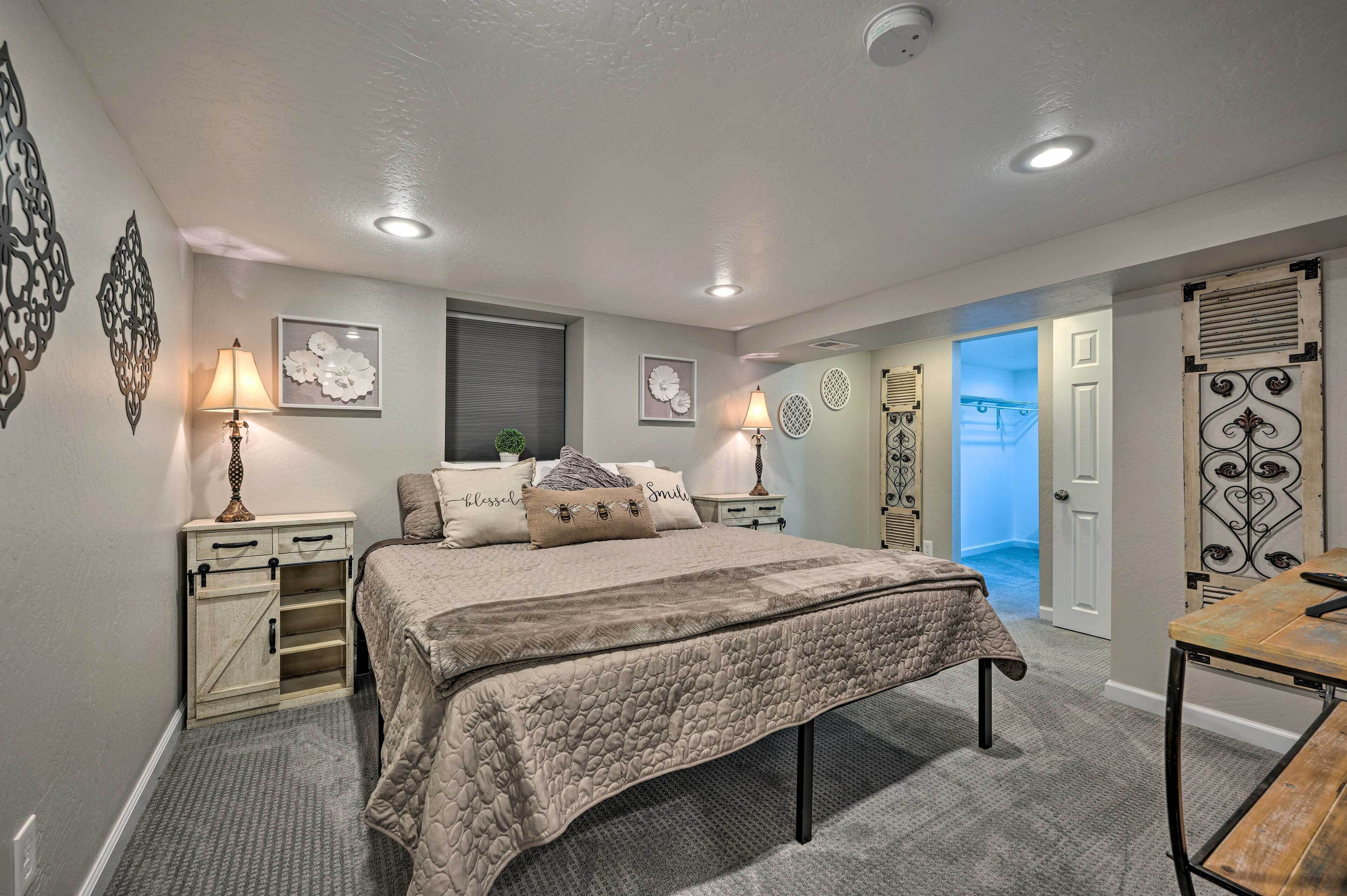 Une chambre à coucher comprenant un lit, des tables de chevet, un bureau et une porte donnant sur une autre pièce.