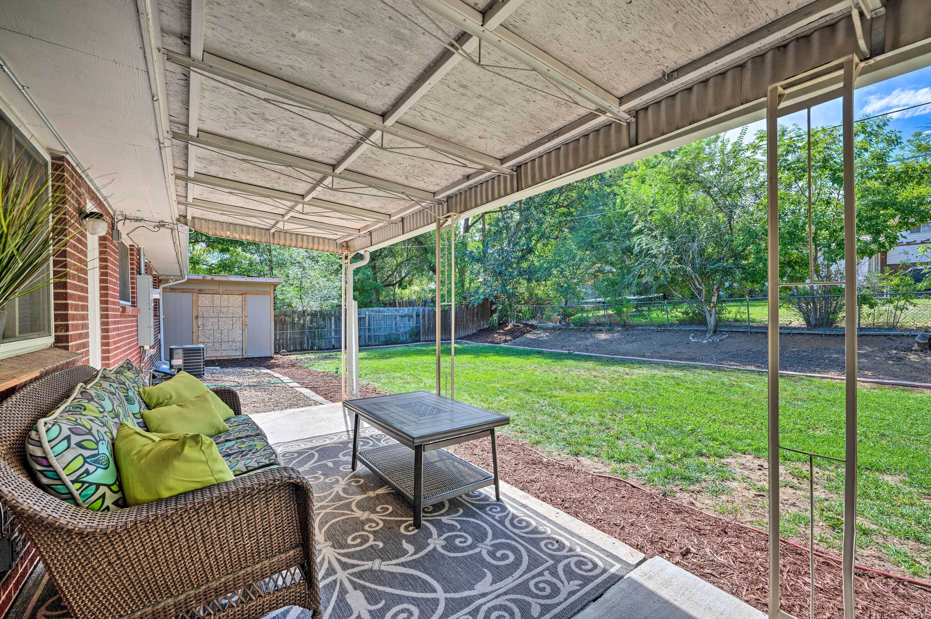 A covered patio area with a wicker sofa, a small table, and a patterned rug.