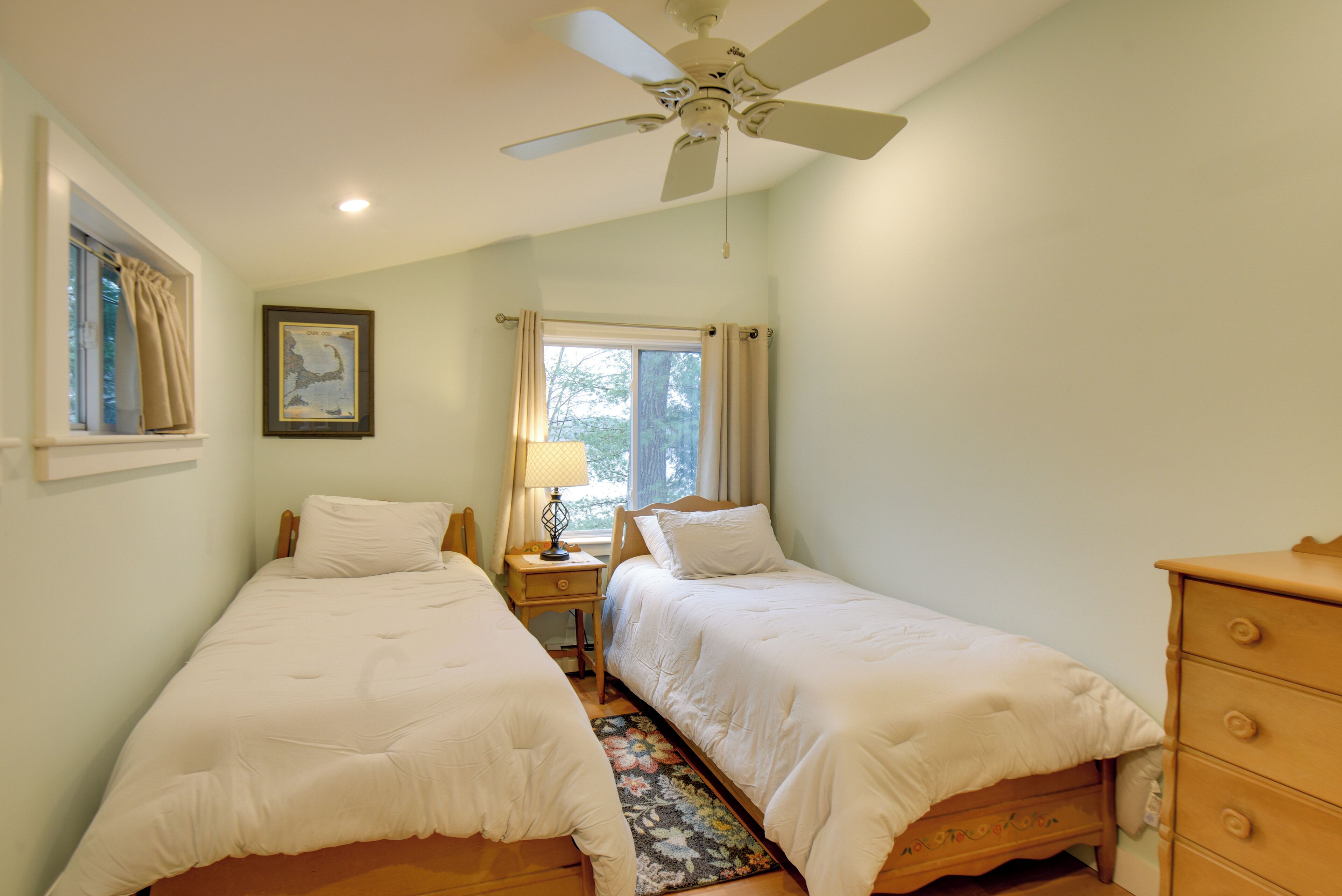 A bedroom with two single beds, a ceiling fan, a nightstand with a lamp, and a dresser.