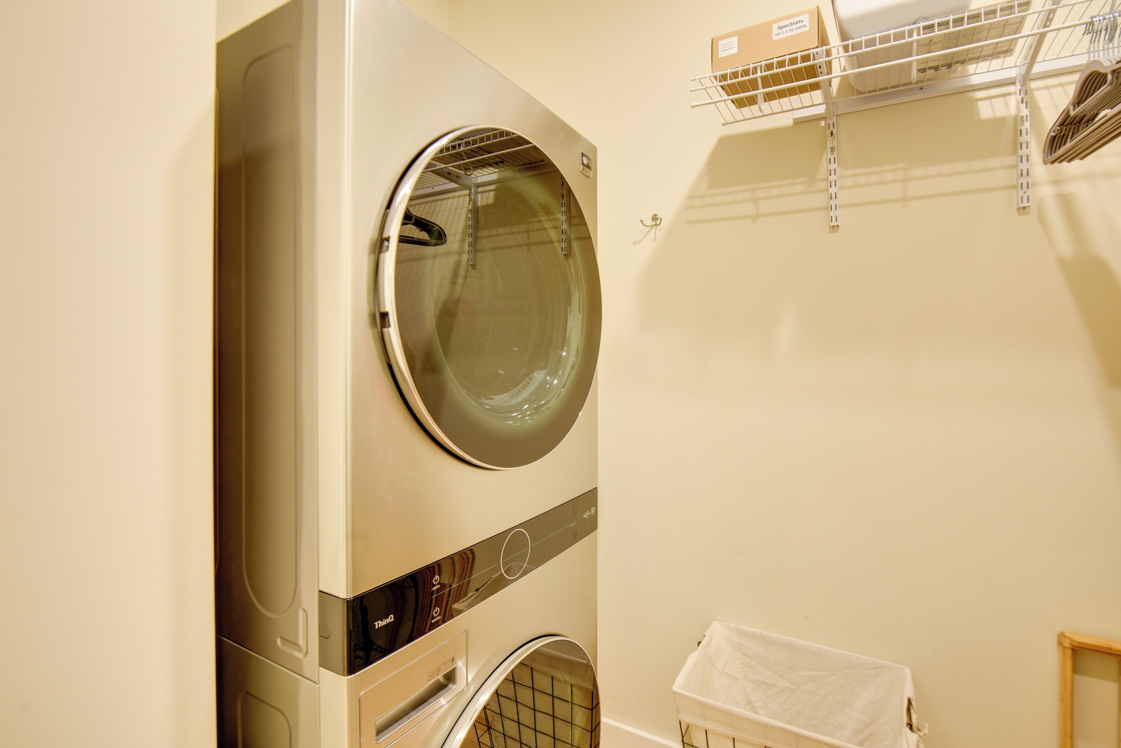 A compact, modern laundry room with a front-loading washer and dryer, a drying rack, and a small storage area with a white basket.