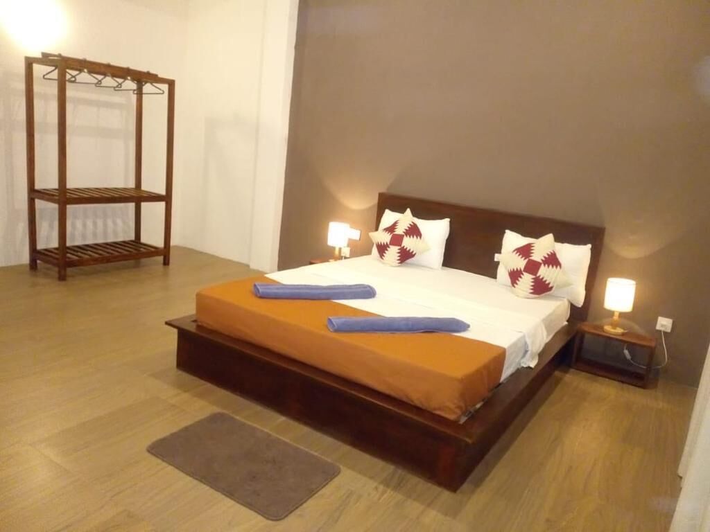 A neatly made bed with a wooden headboard, two bedside lamps, and a small wooden shelf unit.