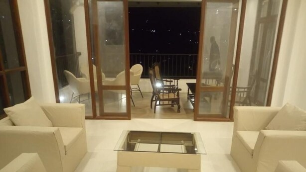 A modern living room with a glass coffee table, white sofas, and a balcony with chairs. - Riverdale Ridge Apartment I (Kandy)