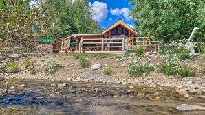 Eine Lodge mit Holzfassade, einer Terrasse und Blick auf einen klaren Bach.