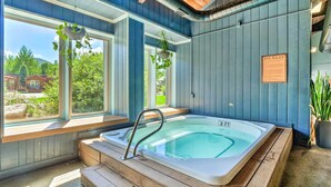 Ein Wellnessraum mit Whirlpool, Holzbänken und großen Fenstern mit Blick ins Freie.