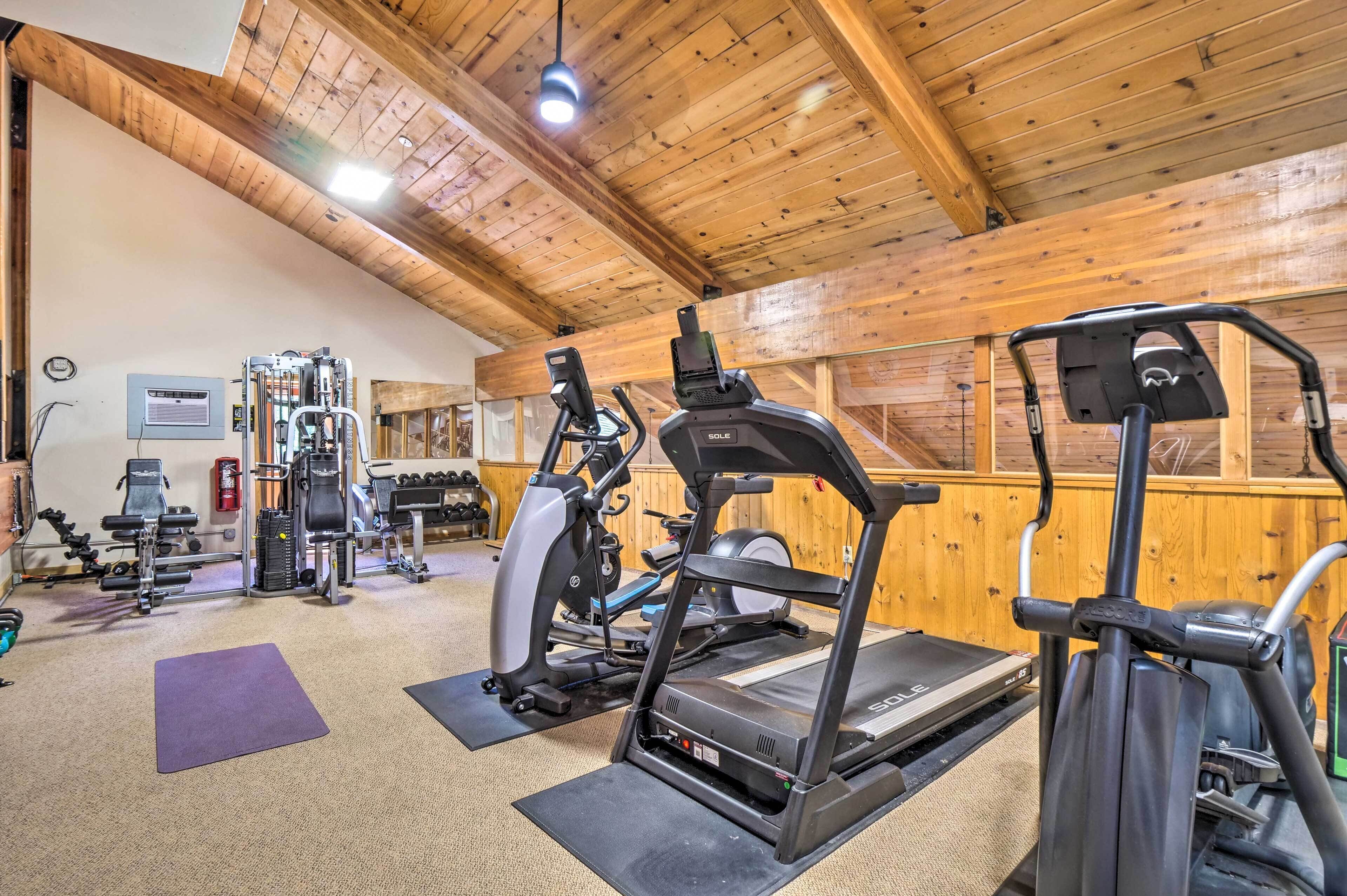 A gym with various exercise equipment, including treadmills and weight machines, in a room with wooden walls and a high ceiling.