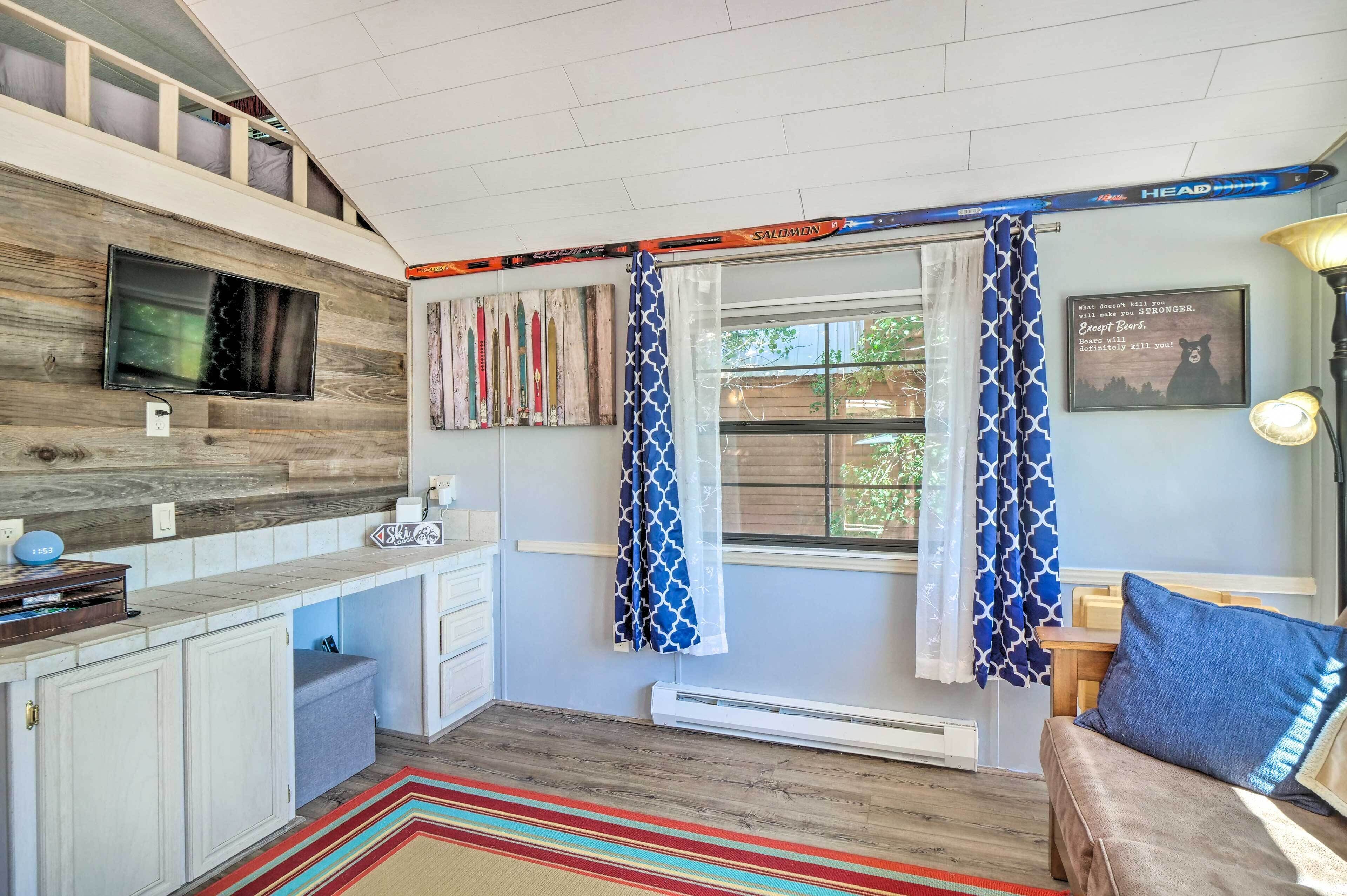 Una habitación acogedora con televisión integrada, una ventana con cortinas estampadas, un cartel motivacional y una alfombra a rayas coloridas.