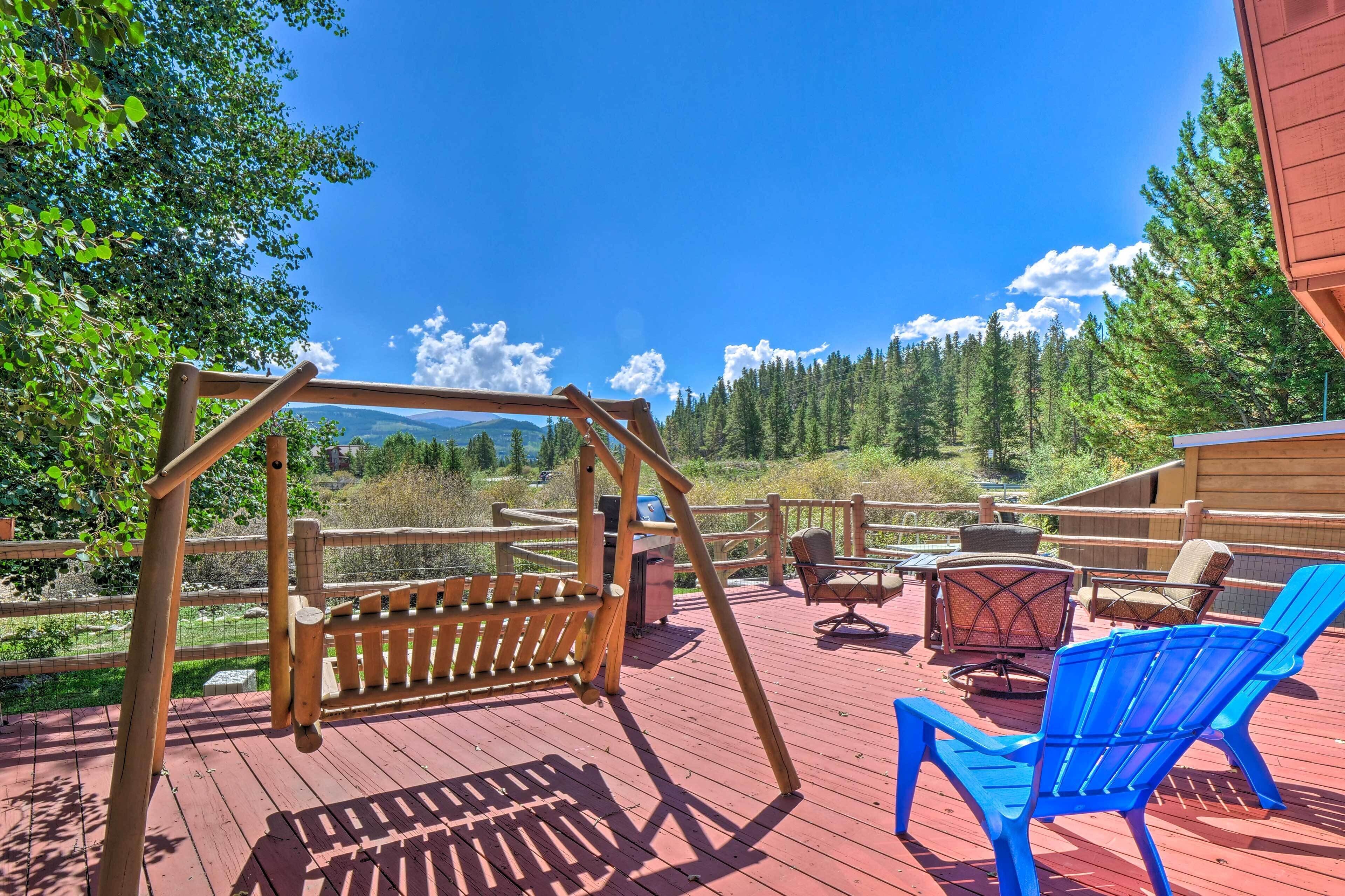 A wooden deck with a swing set, blue chairs, and a table.