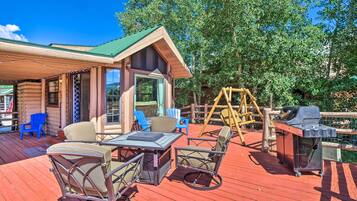 A wooden cabin with a deck, outdoor seating, and a grill.