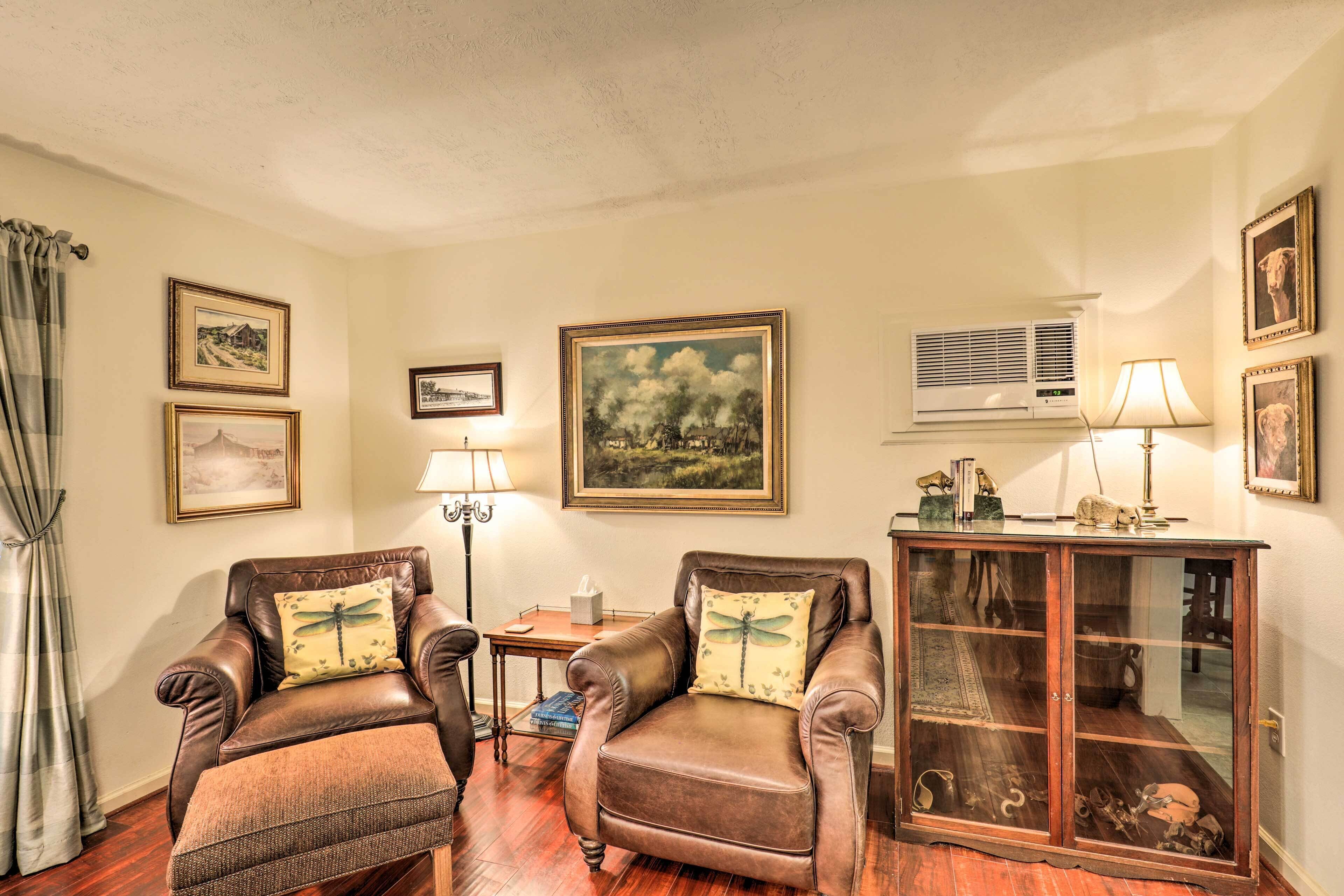 A living room with two leather armchairs, a wooden cabinet, and framed pictures on the walls.