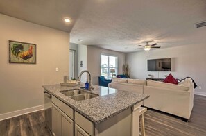 A modern kitchen with granite countertops, a double sink, and a dining area with a white sofa and a TV. - College Station Townhome w/ Furnished Patio! (College Station)