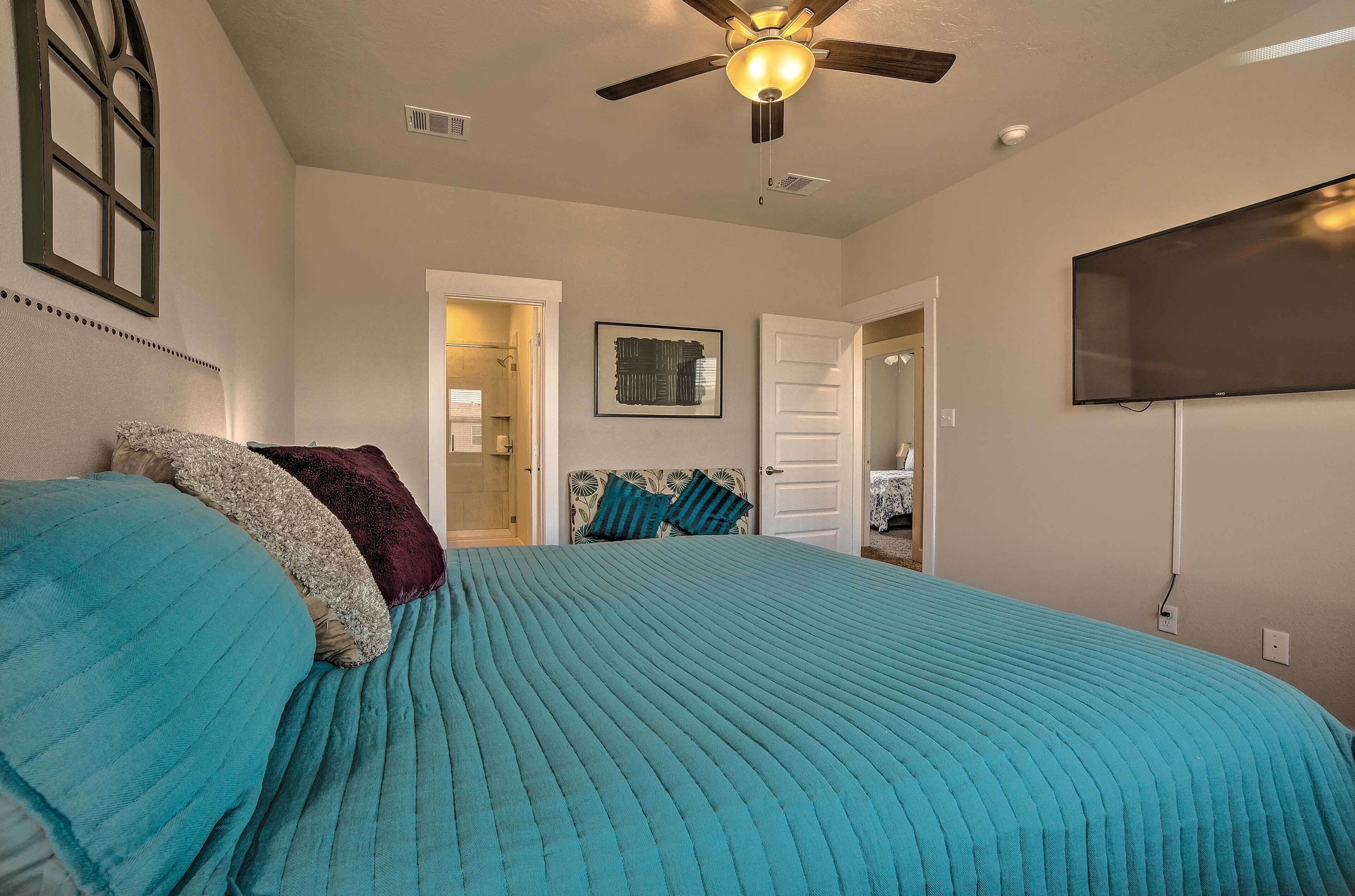 A bedroom with a bed, a ceiling fan, a TV, and a door leading to another room.