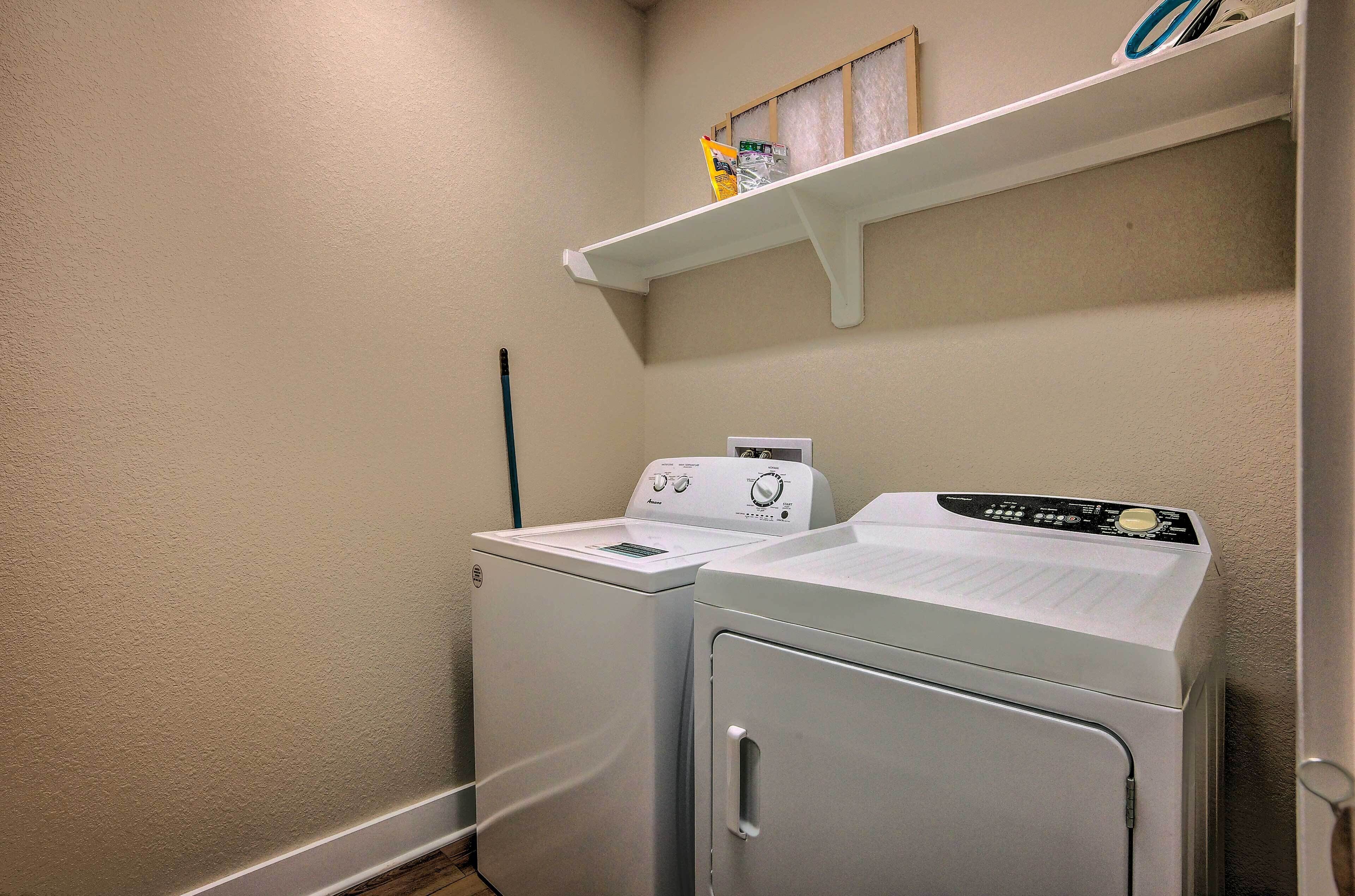 A laundry room with two stacked washers and dryers, a shelf above the dryers, and a wall-mounted vent.