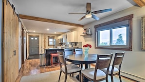A dining area with a round table, four chairs, a ceiling fan, and a window with a view of trees. - Main Street Frisco Condo w/ Private Patio! (Frisco)
