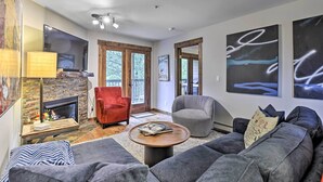 A modern living room with a fireplace, a red armchair, a grey armchair, a grey sofa, and abstract wall art. - Main Street Frisco Condo w/ Private Patio! (Frisco)