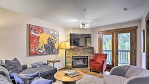 A living room with a fireplace, a large painting, and a red chair. - Main Street Frisco Condo w/ Private Patio! (Frisco)