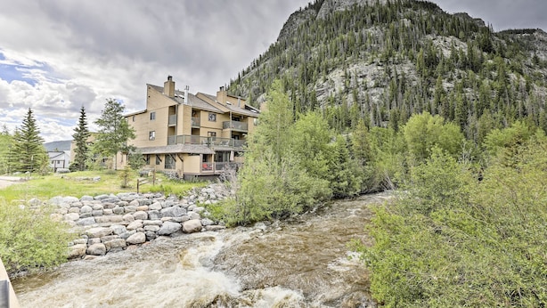 A multi-story building with balconies, a stone retaining wall, and a river in the foreground. - Main Street Frisco Condo w/ Private Patio! (Frisco)