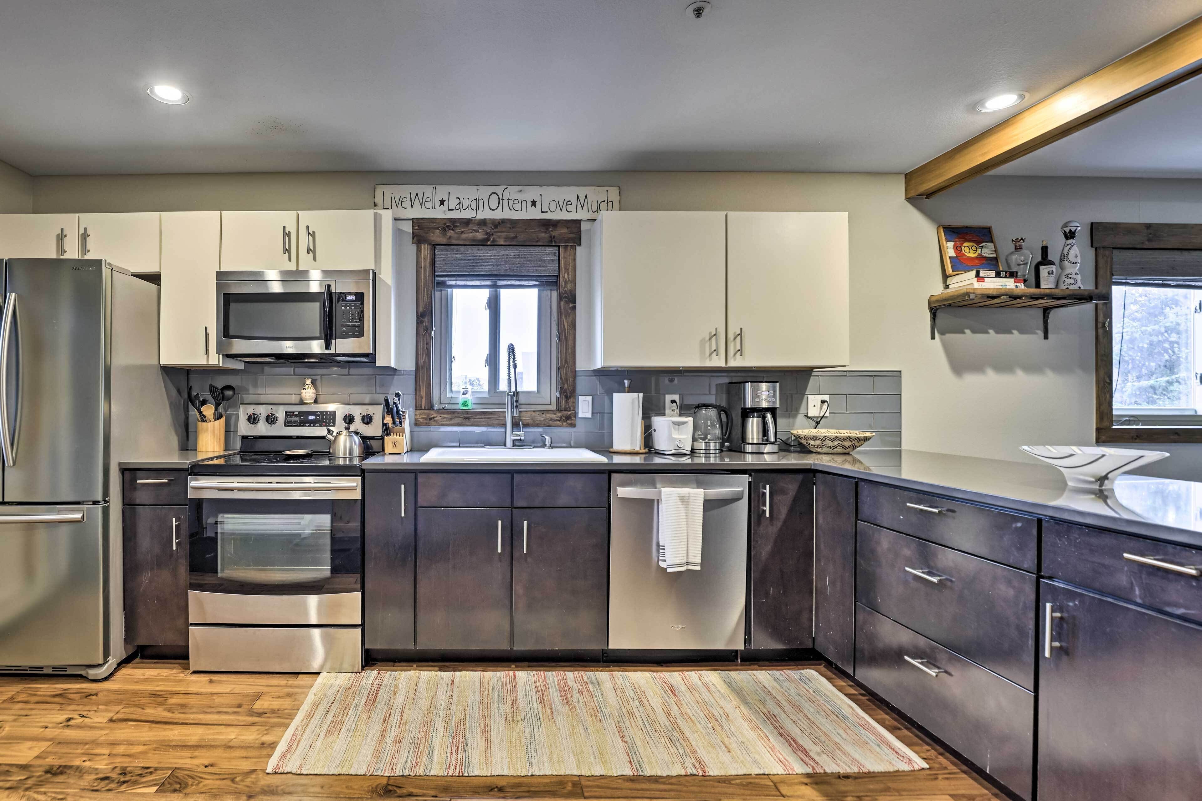 A modern kitchen with stainless steel appliances, dark cabinets, and a wooden floor.