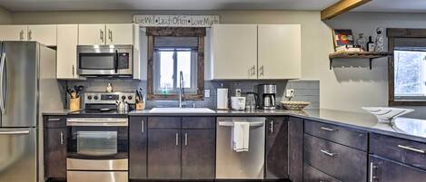 A modern kitchen with stainless steel appliances, dark cabinets, and a wooden floor.