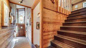 Eine Holztreppe führt zu einer zweiten Etage, begleitet von Holzwänden und einer Tür mit Glasfenster.