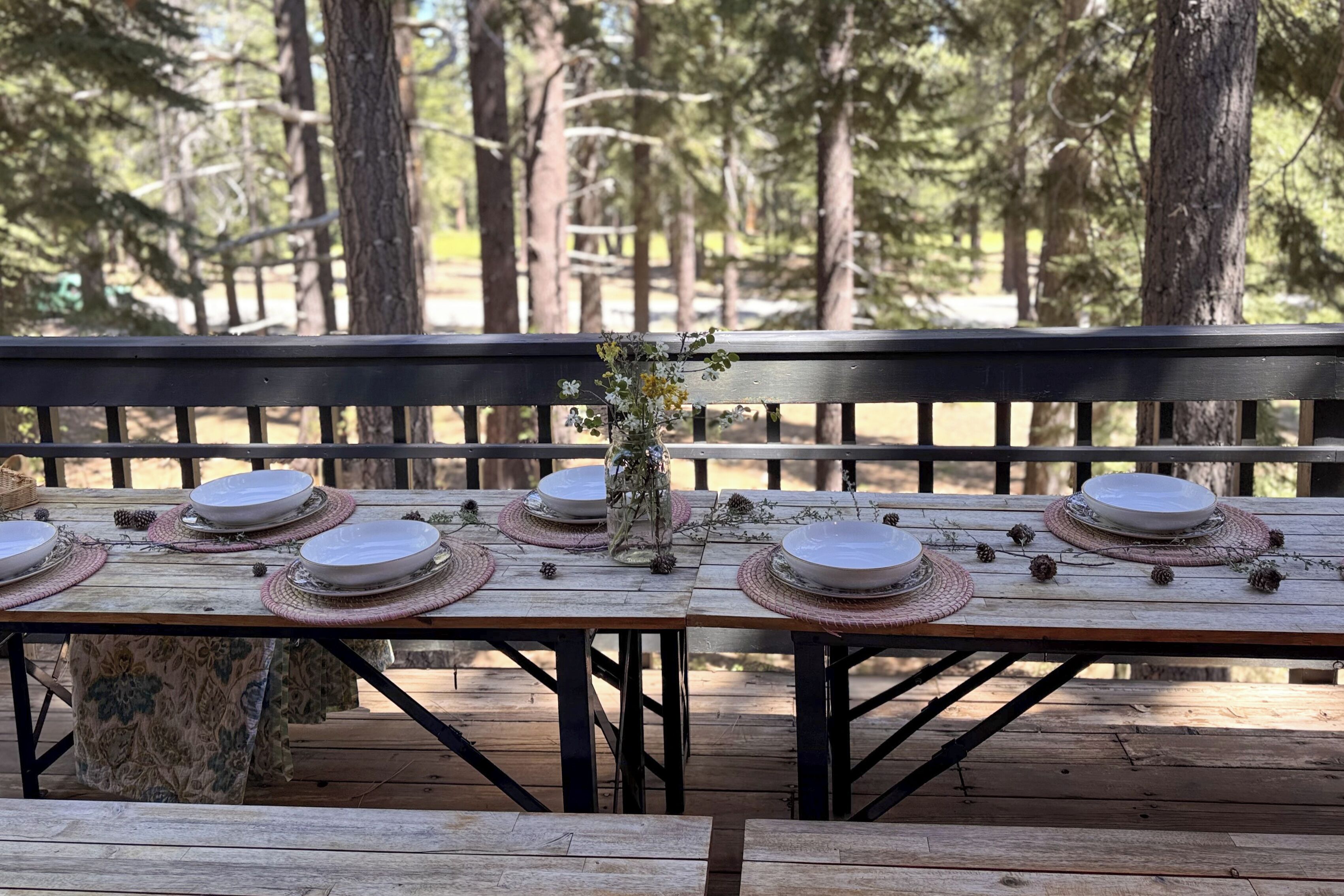 A wooden deck with a table set for a meal, surrounded by trees.