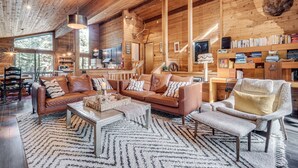 Ein gemütliches Cabin-Interieur mit einer großen Holzbalkendecke, einer Ledersitzgruppe, einem Lesesessel und einem Bücherregal voller Bücher.
