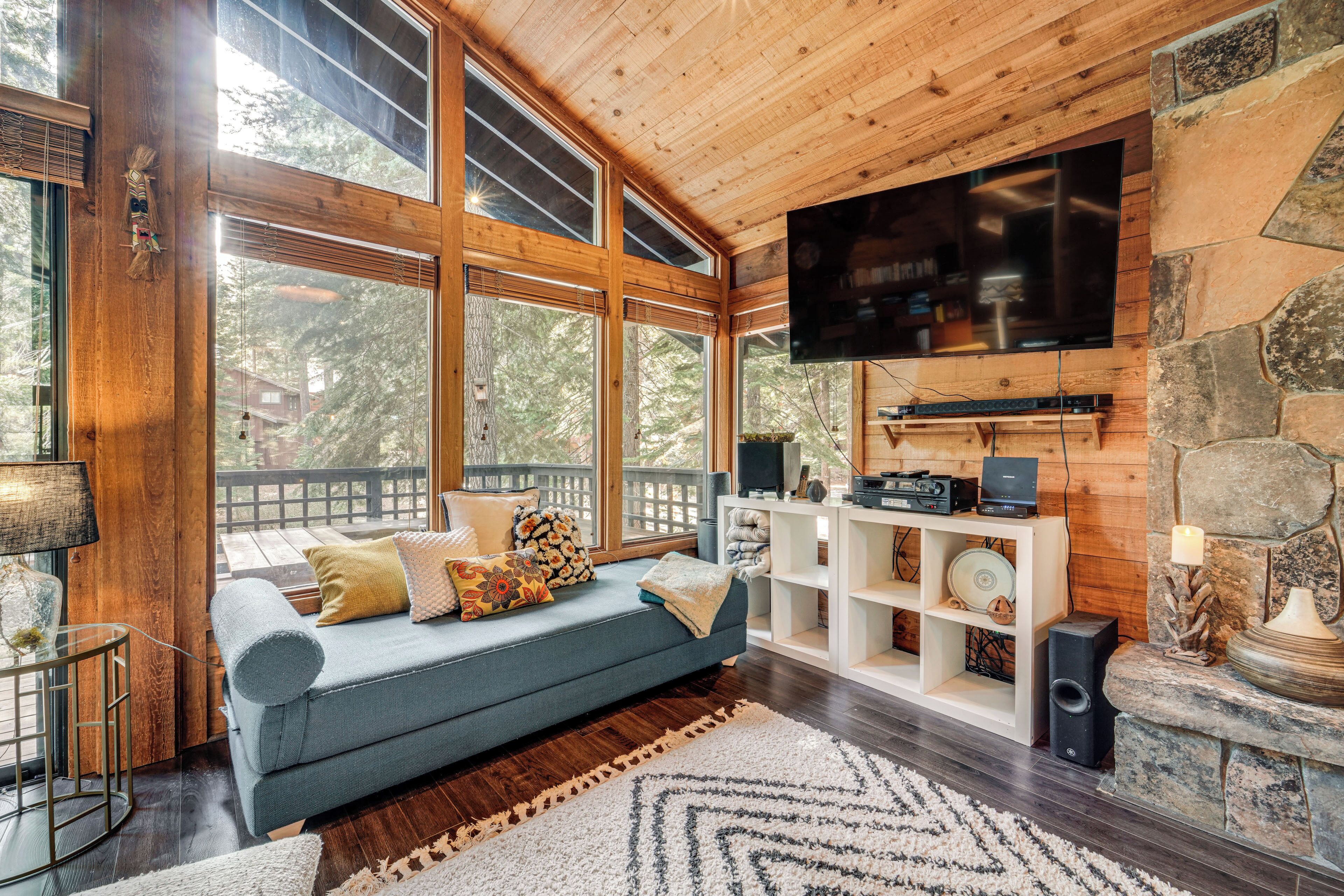 Ein gemütliches Wohnzimmer mit einem blauen Sofa, Holzwänden, einem Steinkamin und einem großen, an der Wand befestigten Fernseher.