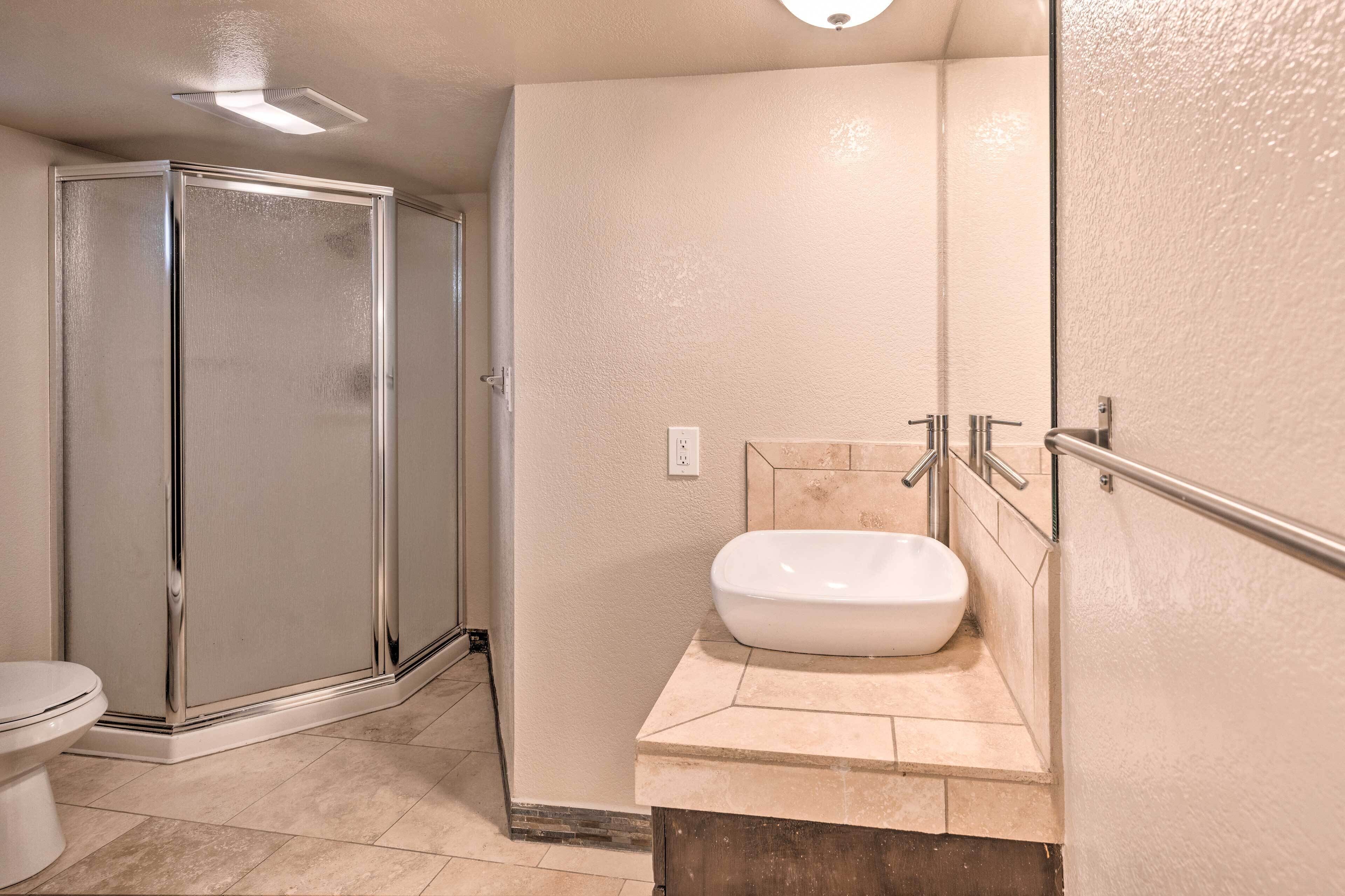 A bathroom with a glass shower enclosure, a white sink with a marble countertop, and a toilet.