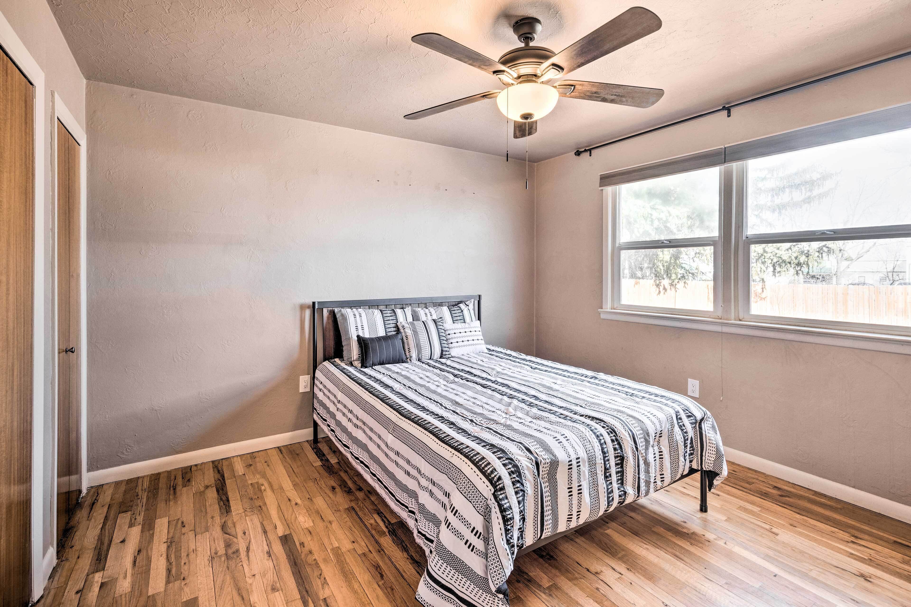 A bedroom with a bed, a ceiling fan, a window, and hardwood flooring.