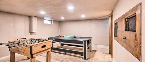 A room with a foosball table, a ping pong table, and a cabinet with a textured glass door.