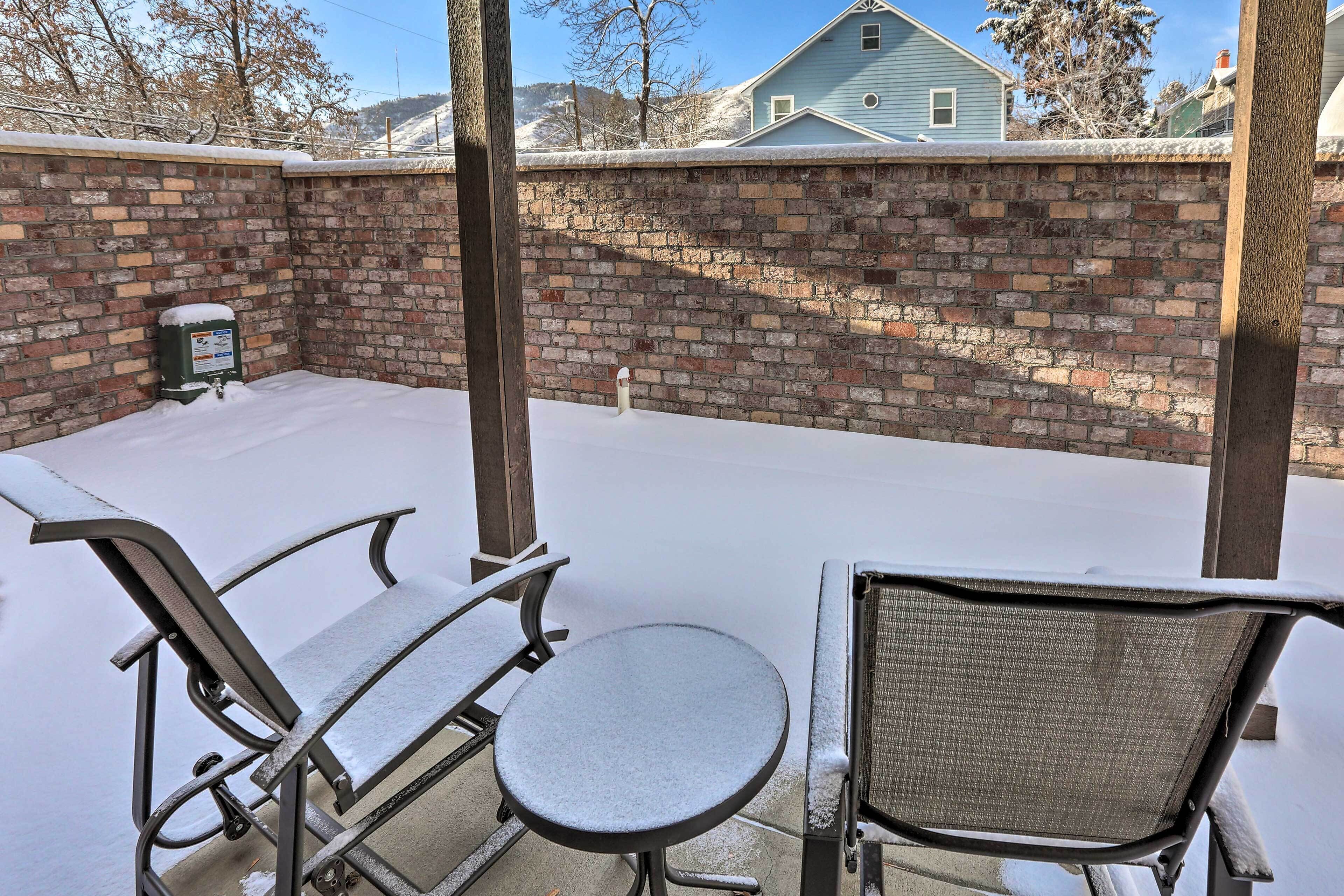 A patio with a brick wall, a metal table, and two metal chairs covered in snow.