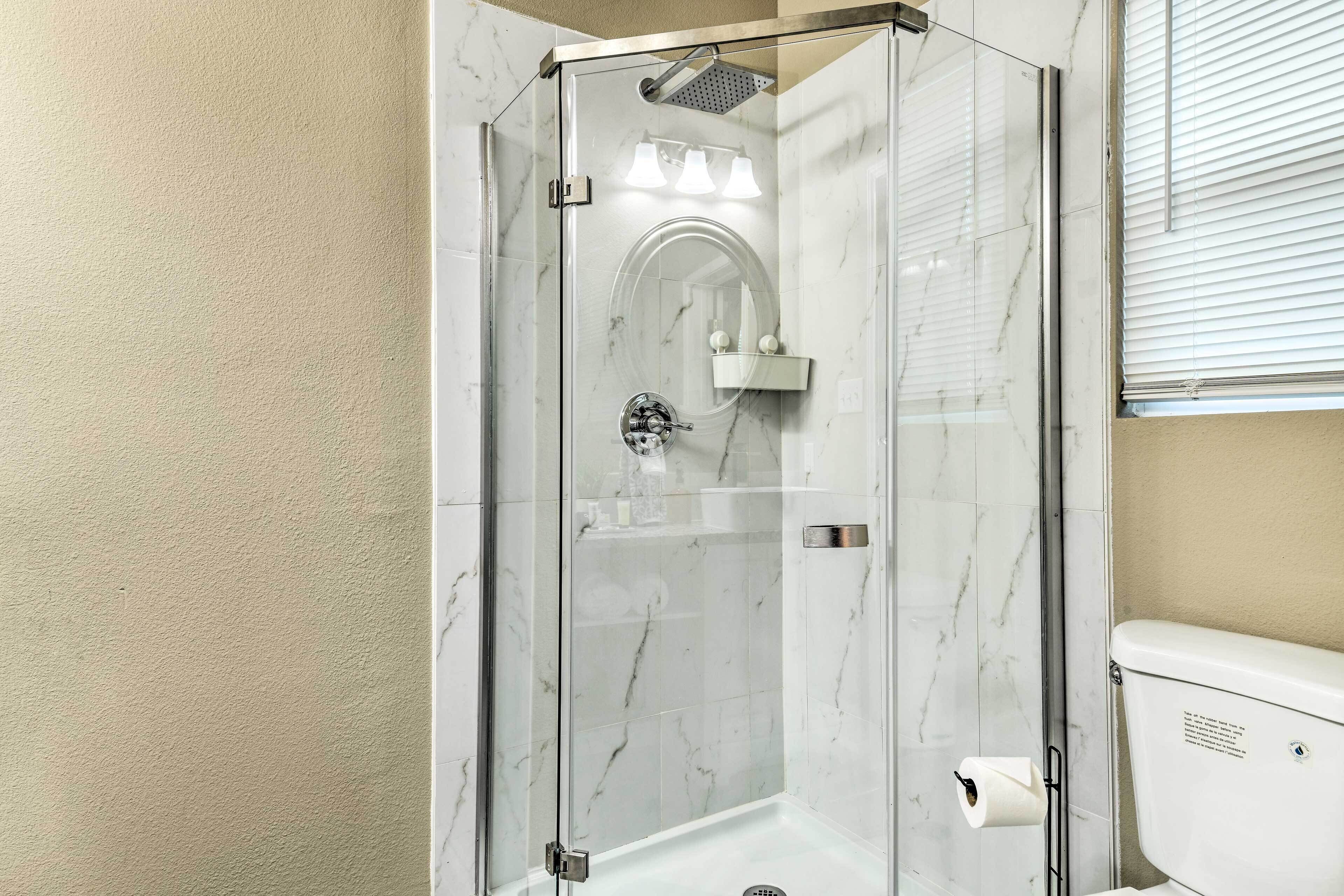 Une salle de bain moderne dotée d’une douche en verre, de murs en marbre et de toilettes avec un porte-serviettes en papier.