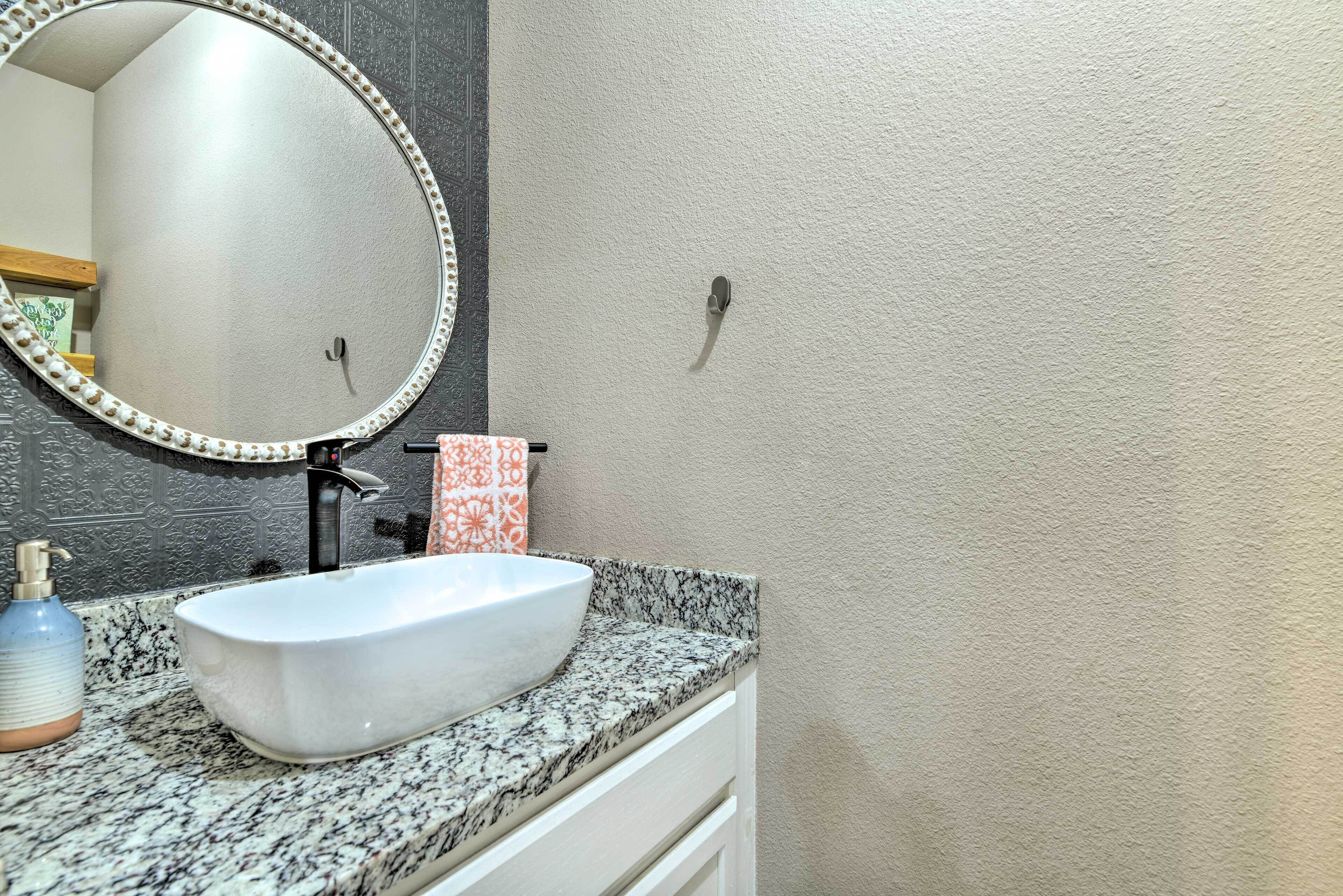 Ein Badezimmer mit einem weißen Waschbecken, einem runden Spiegel mit Perlenrahmen, einem Handtuchspender und einem Seifenspender.