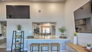A modern kitchen with a central island, wooden stools, and a black metal shelf with plants. - Lakefront Gun Barrel City Home w/ 5 Acres! (Mabank)