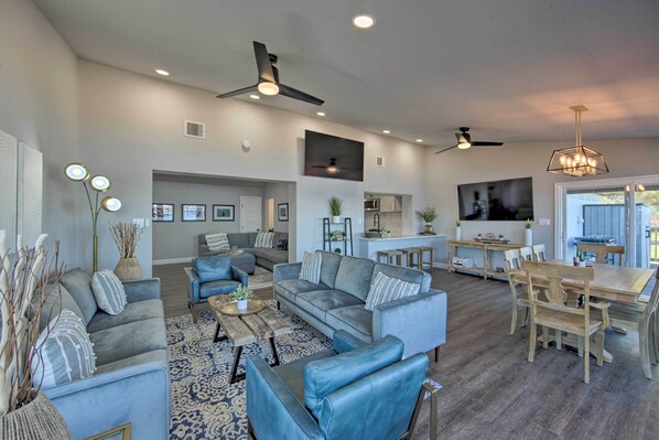 A spacious living room with a large sofa set, a dining area with wooden chairs, and a kitchen in the background.