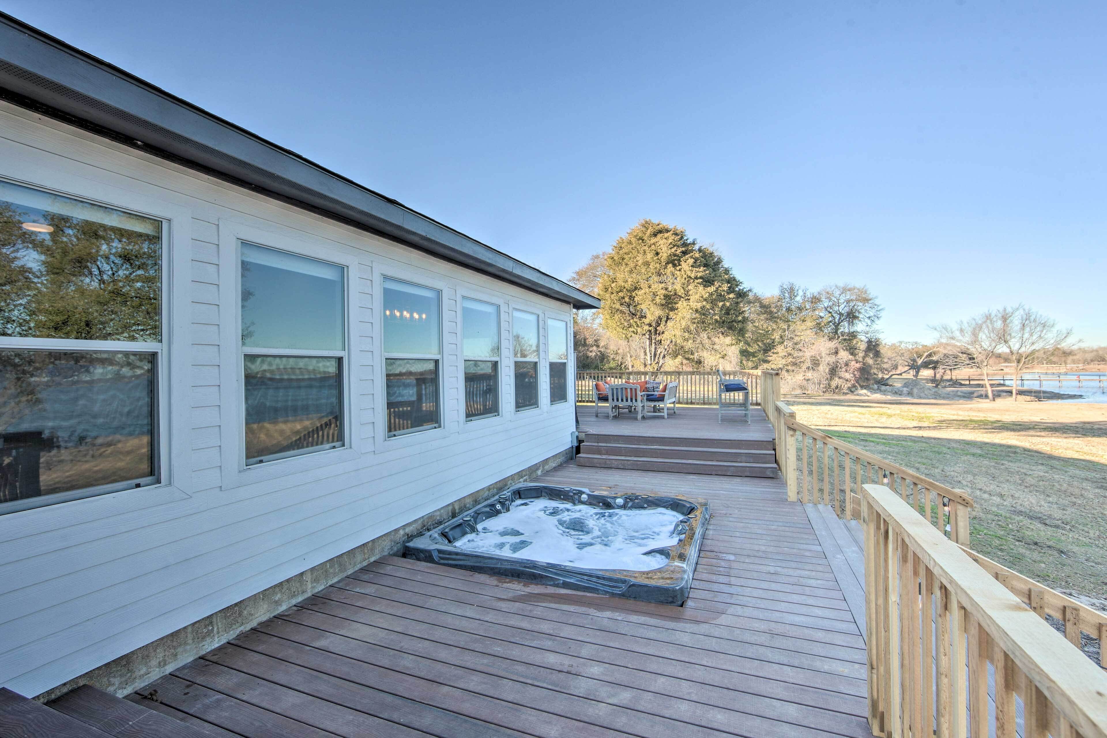 A wooden deck with a hot tub, a covered patio, and a view of a park.