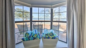 A corner room with a bay window overlooking a deck and a body of water. There are two white cushioned chairs with blue and yellow towels. - Lakefront Gun Barrel City Home w/ 5 Acres! (Mabank)