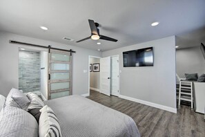 A bedroom with a bed, a ceiling fan, a TV mounted on the wall, and a sliding door.