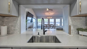 A modern kitchen with a central island, stainless steel sink, and white cabinetry. - Lakefront Gun Barrel City Home w/ 5 Acres! (Mabank)