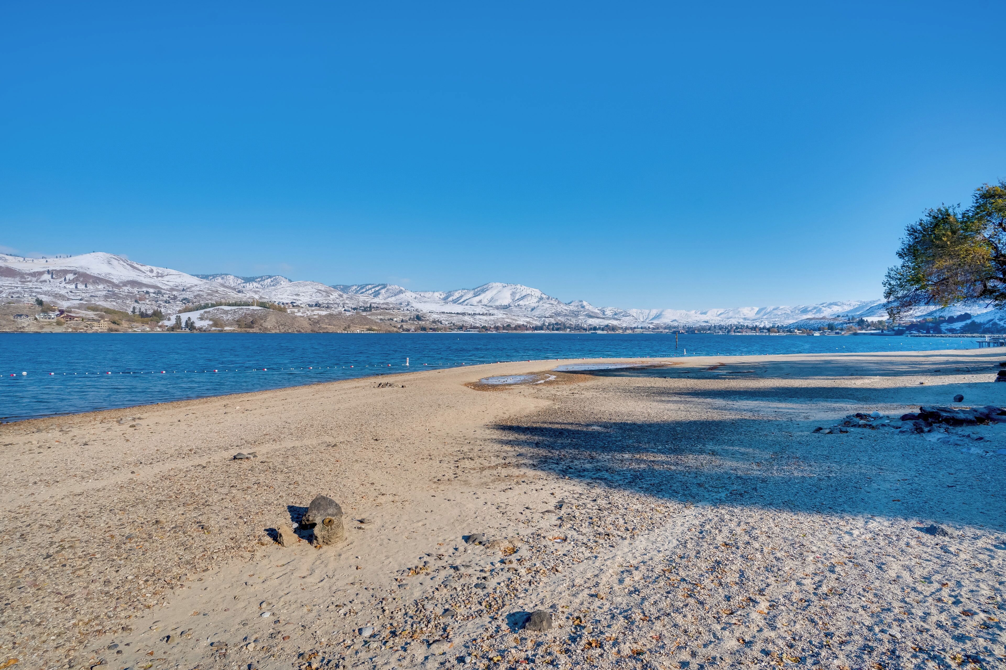 A beach with pebbles and a clear view of snow-capped mountains in the background.