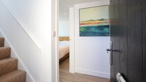 A bedroom with a bed, a wooden floor, and a painting on the wall. - Experience modern coastal living at its finest in this unique one-bedroom property. Sleeps 2. (Dunbar)