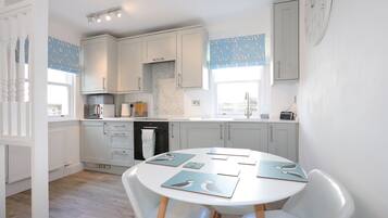 A modern kitchen with white cabinets, a round dining table, and blue patterned window valances.
