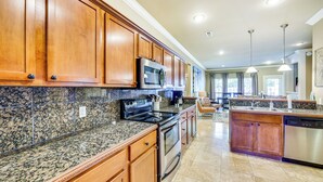A spacious kitchen with granite countertops, wooden cabinets, stainless steel appliances, and pendant lighting.