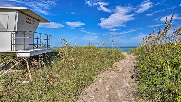 A lifeguard tower with a sign reading "NO GUARD ON DUTY" and a dirt path leading to the beach.