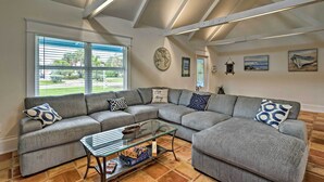 A modern living room with a sectional sofa, a glass coffee table, and a view of the outdoors through large windows.